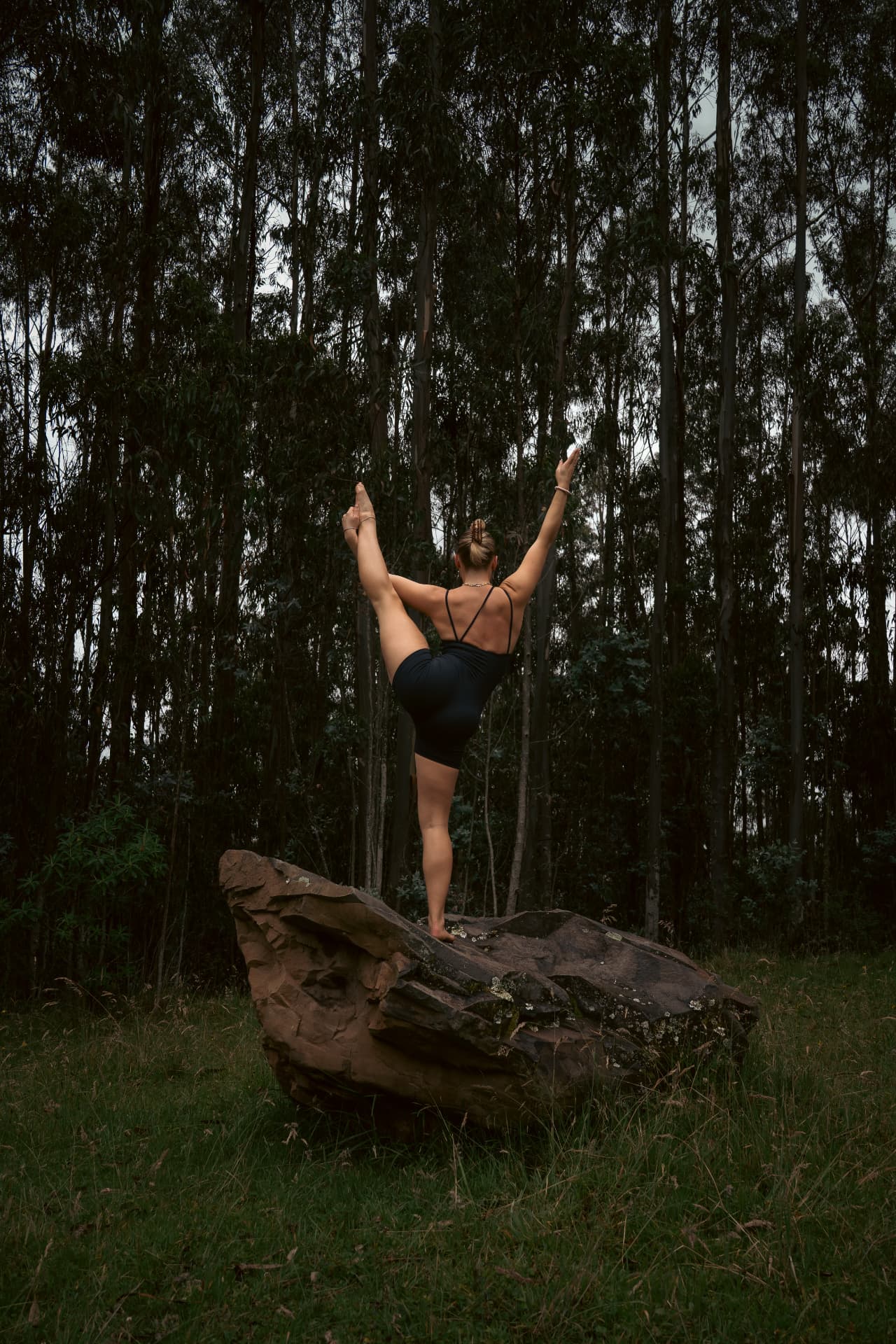 Nora balancing on one leg on a rock in a forest, arms reaching up